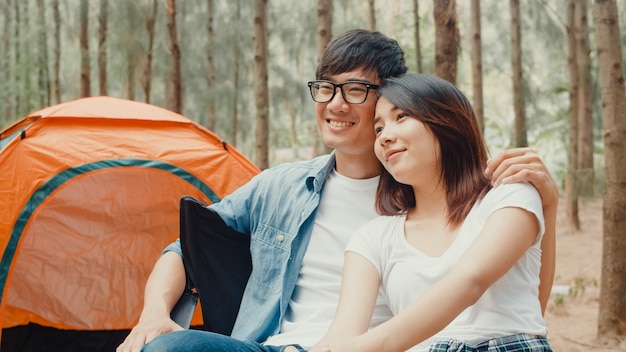 Junges asiatisches Camperpaar sitzt auf Stühlen im Zelt im Wald