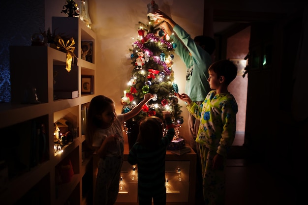 Kinder, die am Abend nach Hause auf den Weihnachtsbaum mit leuchtenden Girlanden schauen.