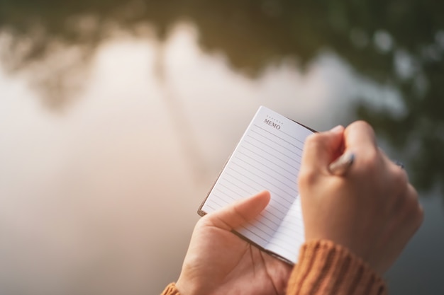 Kopieren Sie den Raum der Frauenhand, die in weißes Notizbuch mit Sonnenlichthintergrund schreibt.