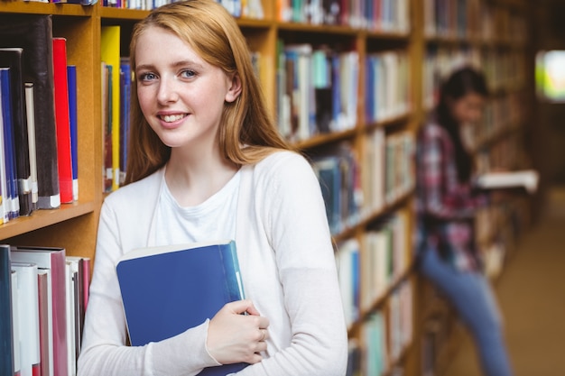 Lächelnder Student, der an den Bücherregalen sich lehnt