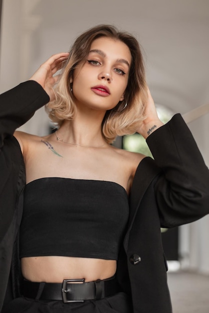 Linda rua fresca modelo de menina bonita com um penteado em roupas de negócios de moda com um top preto e blazer andando na cidade