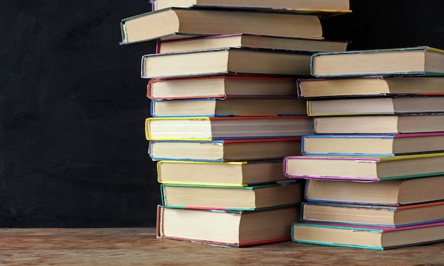 Livros em pilhas na mesa de uma lousa de escola.