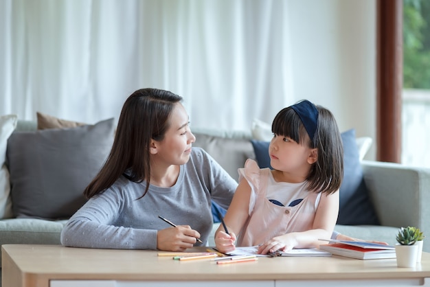 Mãe asiática ensinando sua filha linda a estudar na sala de estar em casa