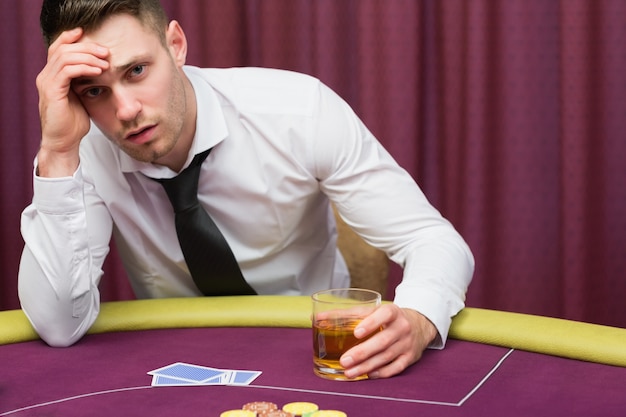 Foto mann, der auf trinkendem whisky der pokertisch sich lehnt