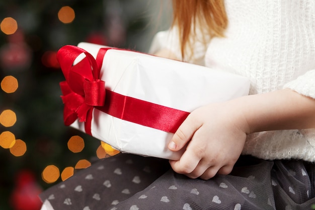 Mãos de criança segurando uma caixa de presente. Natal, ano novo, conceito de aniversário. Fundo festivo com bokeh e luz solar. Conto de fadas mágico