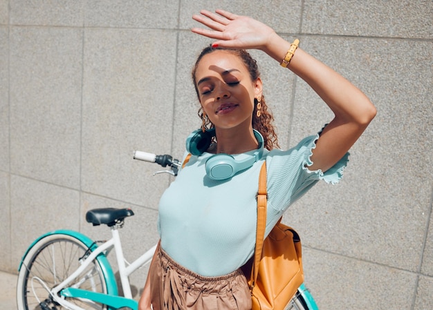 Foto menina da cidade e escudo de mão para exposição ao sol no intervalo de deslocamento ao ar livre na parede de concreto urbano mulher jovem viajante de bicicleta escondendo o rosto da luz solar direta para proteção de sombra no verão