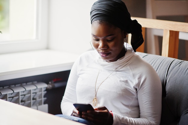 Menina muçulmana africana em hijab preto sentado no café com o celular na mão