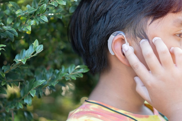 Menino asiático ao ar livre na natureza com aparelho auditivo Tratamento auditivo para um conceito de criança