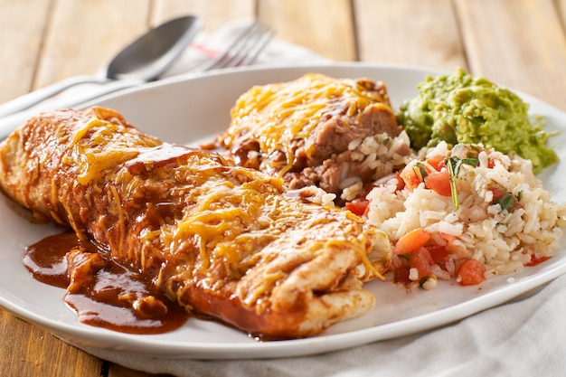 Mexikanische Burritoplatte mit roter Enchiladasauce, gebratenen Bohnen, Reis und Guacamole