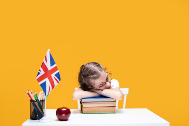 Foto müdes kaukasisches schulmädchen, das am schreibtisch sitzt und englischunterricht schläft großbritannien flagge