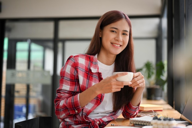 Mulher asiática jovem relaxada relaxando e tomando um chá quente no café