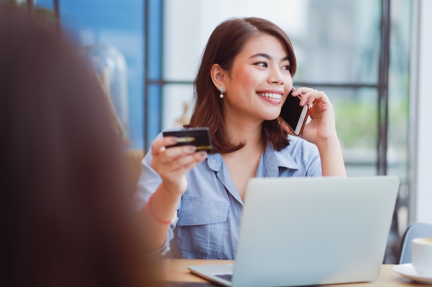 Foto mulher asiática, usando telefone celular com cartão de crédito e computador portátil para fazer compras de pagamento on-line no café café com amigos