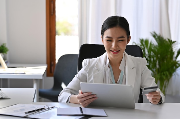 Mulher de negócios asiática atraente fazendo serviços bancários on-line com tablet digital.