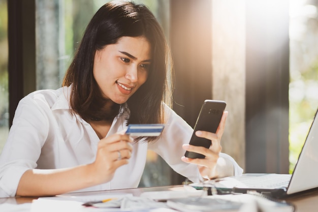 Foto mulher de negócios sorridente segurando cartão de crédito e telefone celular na mesa no escritório