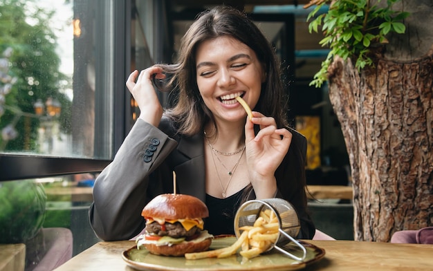 Mulher jovem e atraente comendo batatas fritas e um hambúrguer em um restaurante