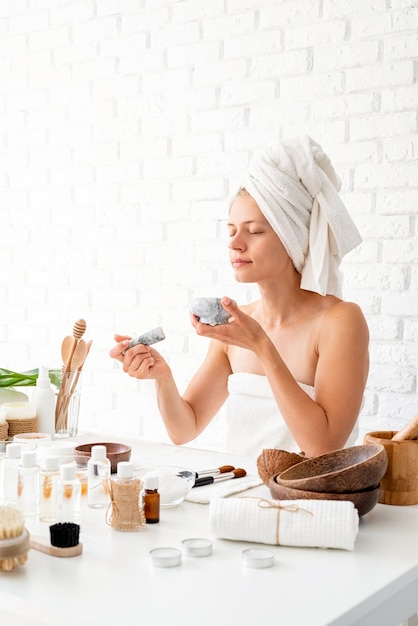 Foto mulher jovem feliz vestindo roupas de banho brancas toalhas na cabeça fazendo procedimentos de spa misturando natural