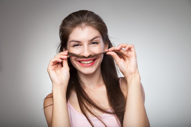 Mulher morena sorridente segurando o cabelo dela e mostrando o bigode. Tiro do estúdio.