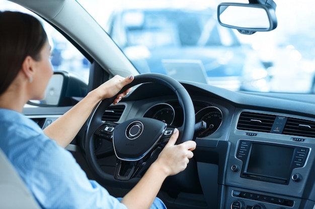 Mulher sentada em um carro novo no salão segurando um volante