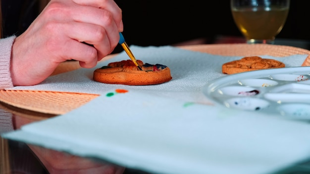 Nahaufnahme von Frauenhänden, die Lebkuchen in der Küche malen, Frau, die Kekse verziert