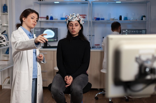 Foto neurologe arzt zeigt monitor mit gehirnaktivität für patientin mit eeg-scanner auf dem kopf während des neurowissenschaftlichen experiments im medizinischen labor. wissenschaftler arzt analysiert die entwicklung des nervensystems