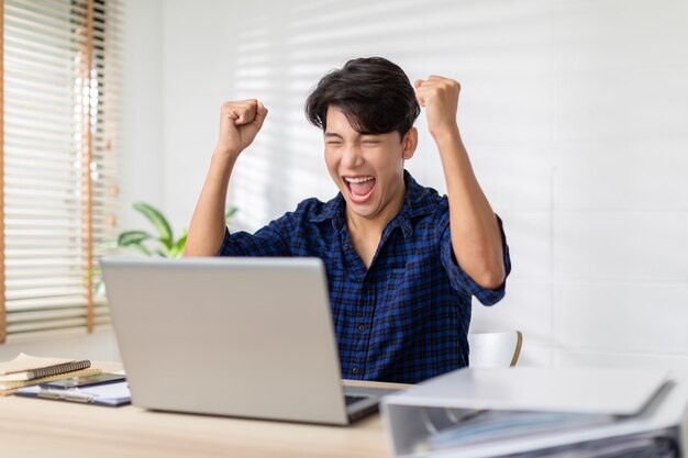 Foto o homem asiático está sorrindo e expressando sentimento de felicidade na tela do computador laptop jovem homem recebeu boas notícias e mostrar o seu rosto alegre felicidade homens olhando para o laptop ler mensagem se sentir entusiasmado em casa