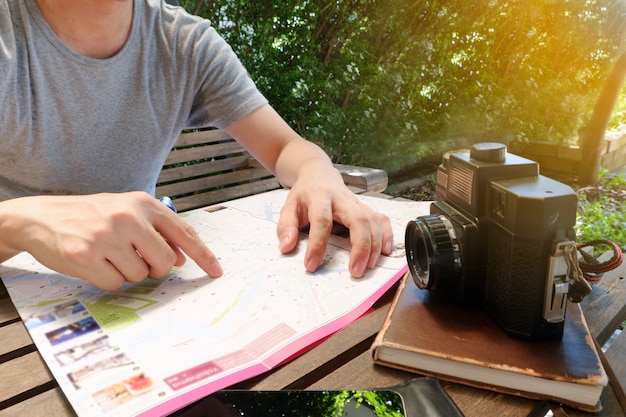 O viajante do homem está procurando algum lugar no mapa local, enquanto relaxa no café, com leve conceito de manhã, viagem e recreação