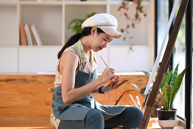 Foto pacífica jovem artista feminina pintando imagens no estúdio de arte.