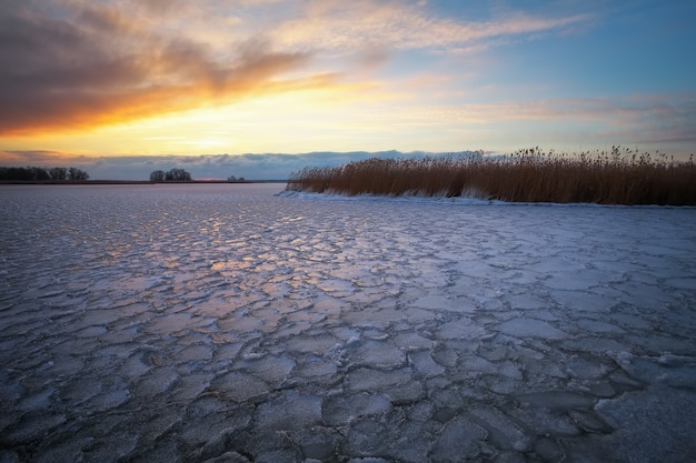 Paisagem do inverno com lago congelado e céu pôr do sol. Composição da natureza.