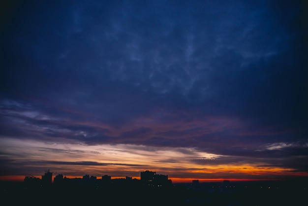 Foto paisagem urbana com amanhecer quente vívido. céu dramático violeta azul dramático surpreendente acima das silhuetas escuras dos edifícios da cidade. luz do sol laranja.