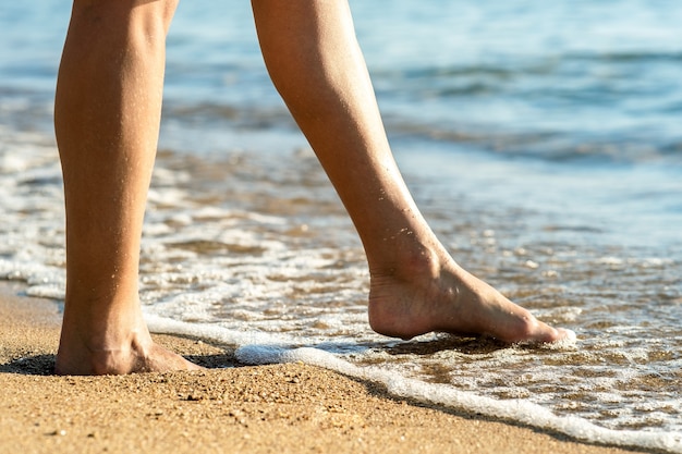 Perto dos pés de uma mulher caminhando descalça na praia de areia na água do mar