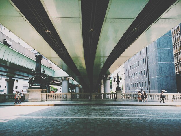 Foto pessoas a caminhar na calçada debaixo da ponte.