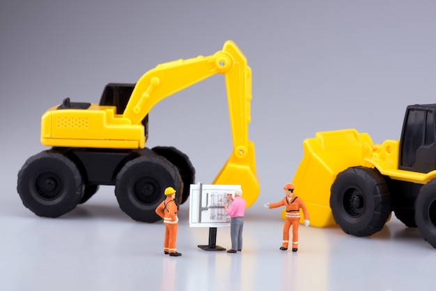 Pessoas de engenharia em miniatura e máquinas trabalhando no desenho de construção