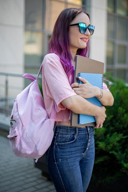 Porträt einer schönen Schriftstellerin in lässigem Outfit, die einen modernen Laptop mit Rucksack in der Hand hält