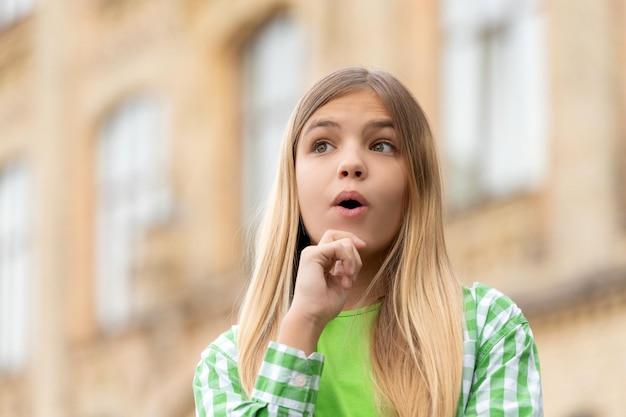 Porträt eines Teenager-Mädchens mit überraschtem Gesicht, das mit dem Kinn auf der Hand wegschaut, verschwommener Kopierraum im Freien