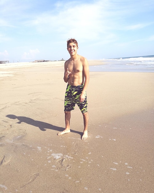 Foto portrait in voller länge eines hemdlosen jungen, der am strand steht