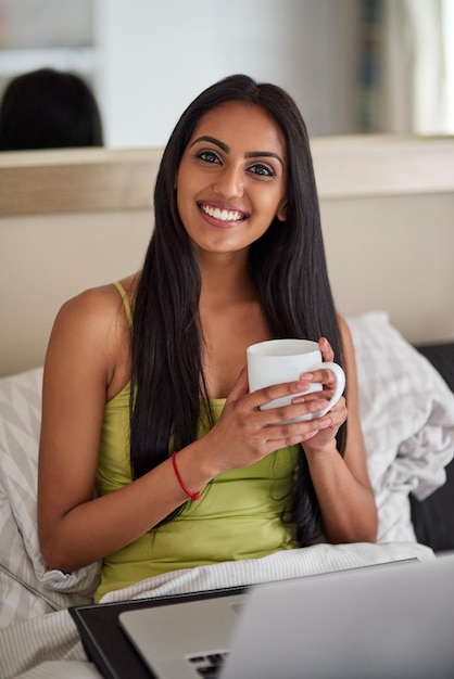 Quem precisa sair da cama com internet de alta velocidade Foto de uma jovem relaxada usando um laptop e tomando café na cama