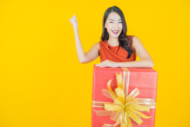 Retrato de uma bela jovem asiática sorrindo com caixa de presente vermelha em amarelo