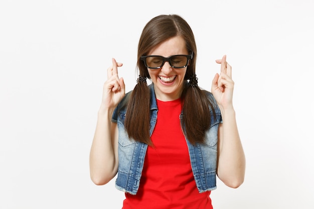 Retrato de uma jovem mulher bonita feliz em óculos 3d e roupas casuais, assistindo a um filme, mantendo os dedos cruzados e os olhos fechados, isolados no estúdio em fundo branco. Emoções no conceito de cinema.