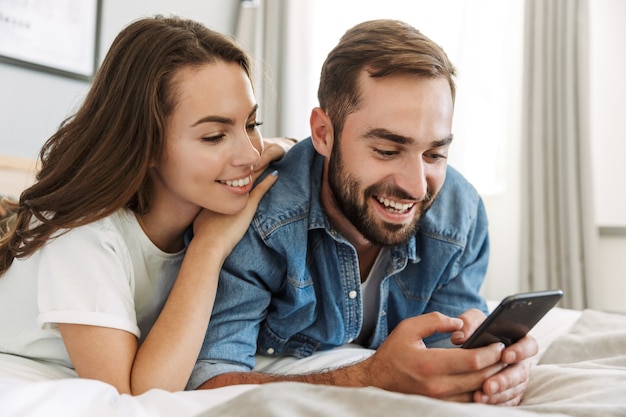 Schönes junges verliebtes Paar zu Hause, im Bett liegend, mit Handys