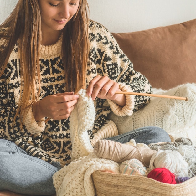 Foto schönes mädchen strickt einen warmen pullover auf dem bett. stricken als hobby. zubehör zum stricken.