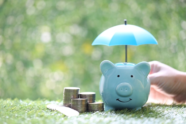 Foto schutz, sparschwein mit hand, die den regenschirm und münzstapel auf natürlichem grünem hintergrund hält, finanzversicherung und sicheres anlagekonzept investment