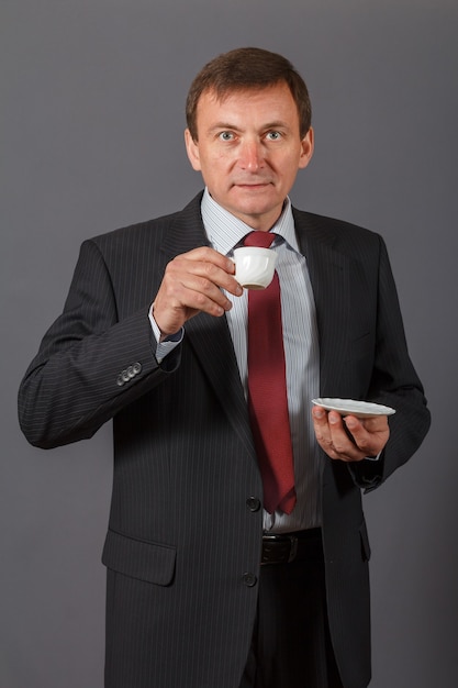 selbstbewusster und freundlicher, eleganter, gutaussehender reifer Geschäftsmann, der eine Tasse Kaffee trinkt