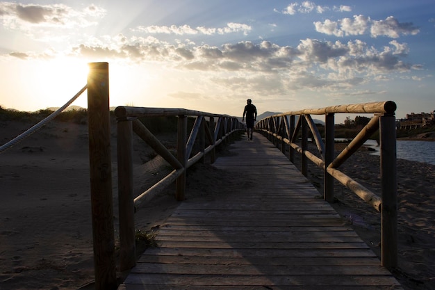 Silhouette eines Mannes, der bei Sonnenuntergang auf einem Holzsteg geht