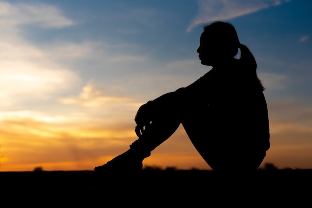 Silhueta de mulheres tristes e deprimidas sentadas na passarela do parque com o pôr do sol