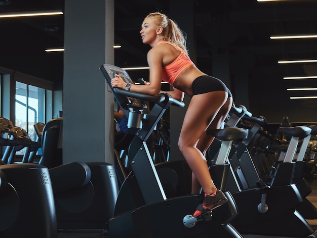 Sportliche blonde Frau, die in einem modernen Fitnesscenter auf einem Heimtrainer trainiert. Fitness-Lifestyle im Sportverein.