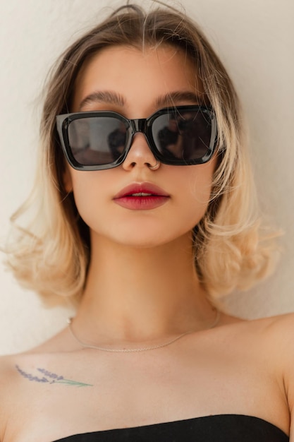 Städtisches weibliches sommerfrisches Porträt eines schönen jungen Frauenmodells mit cooler Sonnenbrille in schwarzem Spitzenständer auf weißem Hintergrund auf der Straße