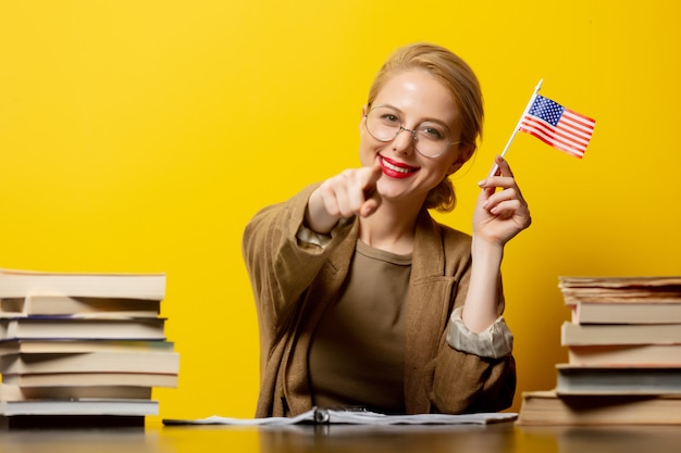 Foto stil blonde frau, die am tisch mit büchern herum sitzt und usa-flagge auf gelb hält