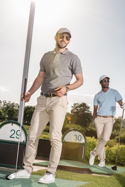 Foto stilvolle spieler mit golfschlägern in den händen, die auf dem golfplatz stehen