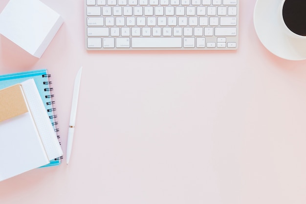 Tastatur und Kaffeetasse nahe Briefpapier auf rosa Schreibtisch