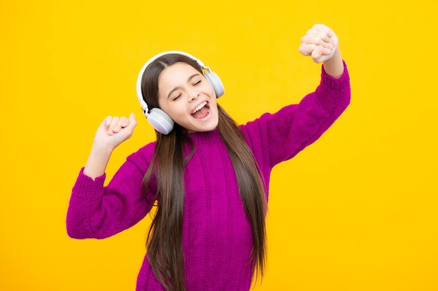 Teenager-Mädchen mit Kopfhörern, die Musik hören und stilvolles, lässiges Outfit tragen, isoliert auf gelbem Hintergrund